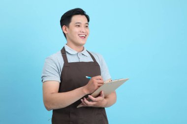 Garson üniformalı Asyalı yakışıklı adam, hoş geldin misafir ve sipariş, mavi arka planda izole.