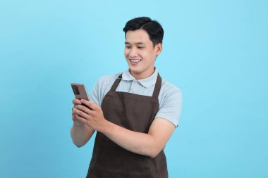 Garson üniformalı Asyalı yakışıklı adam, hoş geldin misafir ve sipariş, mavi arka planda izole.