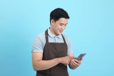 Garson üniformalı Asyalı yakışıklı adam, hoş geldin misafir ve sipariş, mavi arka planda izole.
