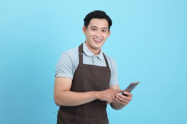 Garson üniformalı Asyalı yakışıklı adam, hoş geldin misafir ve sipariş, mavi arka planda izole.