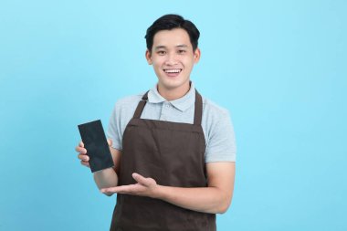 Garson üniformalı Asyalı yakışıklı adam, hoş geldin misafir ve sipariş, mavi arka planda izole.