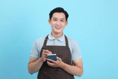 Garson üniformalı Asyalı yakışıklı adam, hoş geldin misafir ve sipariş, mavi arka planda izole.