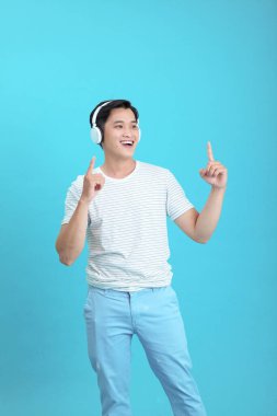 Asyalı yakışıklı ve neşeli genç adam müzik dinliyor, arka planda soyutlanmış