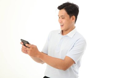 Asyalı yakışıklı ve neşeli genç adam oyun oynuyor ya da arka planda izole bir şekilde akıllı telefondan video izliyor.