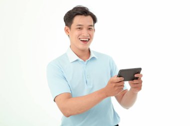 Asyalı yakışıklı ve neşeli genç adam oyun oynuyor ya da arka planda izole bir şekilde akıllı telefondan video izliyor.