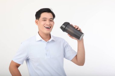 Asyalı yakışıklı genç ve neşeli bir adamın fotoğrafı beyaz arka planda izole edilmiş beyaz bir şişe süt proteini tutuyor.