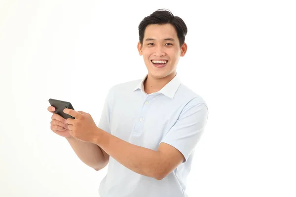アジアのハンサムで陽気な若い男がゲームをプレイしたり スマートフォンでビデオを見て 背景に隔離された — ストック写真