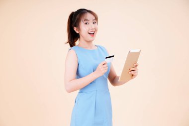 Asyalı genç, güzel ve neşeli bir kadının portresi kredi kartıyla çevrimiçi ödeme yapıyor.