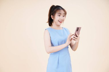 Asyalı güzel ve neşeli bir kadının portresi. Akıllı telefon kullanıyor, arka planda izole edilmiş.