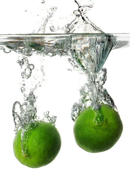 Limes salpicando em água — Fotografia de Stock