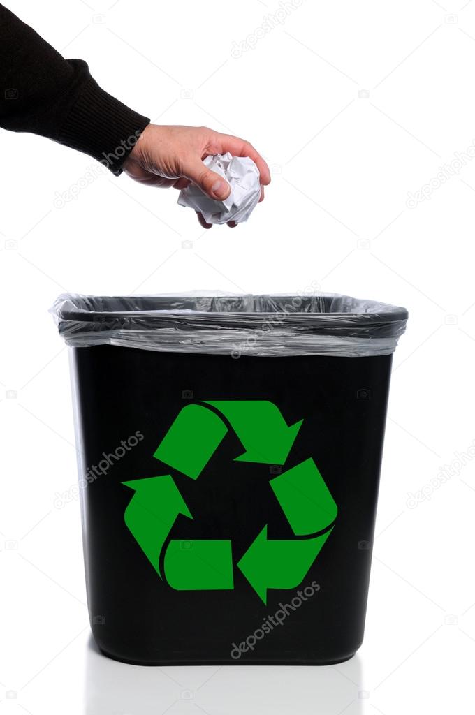 Man's hand placing paper in trash can with recycle symbol