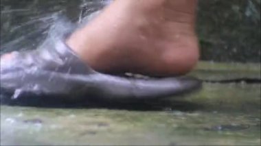 Ayaklar musluktan suyla yıkanırken, su ağır çekimde musluktan akar, ayaklar sandaletle yıkanır.