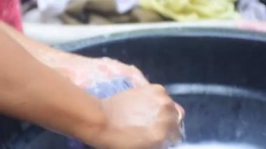 Asyalı kadın çamaşır yıkıyor. Yıkama ve fırçalama, yüksek çözünürlüklü video. Endonezyalı kadın banyonun yanında çamaşır yıkıyor. Sabun köpüklü kovada el yıkama kıyafetleri.