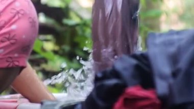 Asyalı kadın çamaşır yıkıyor. Yıkama ve fırçalama, yüksek çözünürlüklü video. Endonezyalı kadın banyonun yanında çamaşır yıkıyor. Sabun köpüklü kovada el yıkama kıyafetleri.