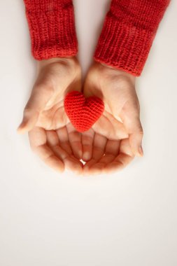 Kırmızı kazaklı bir adam avuçlarında kırmızı bir kalp taşıyor. Sevgililer Günü bayramı sembolü