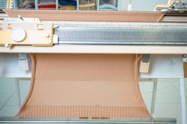 Bir örgü makinesine sıcak karamel bej örülmüş kumaş. Örgü makinesinde bir şeyler yapma süreci. İş olarak örgü örüyorum. Yüksek kalite fotoğraf