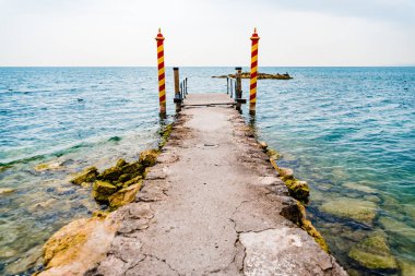 San Vigilio 'nun ucundaki eski taş iskelede, Lago di Garda' da renkli demirleme direkleriyle