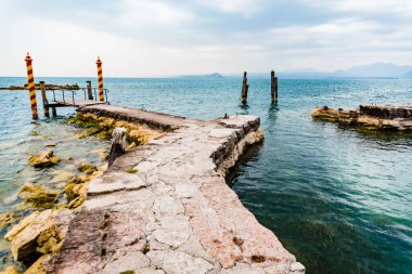 San Vigilio 'nun ucundaki eski taş iskelede, Lago di Garda' da renkli demirleme direkleriyle