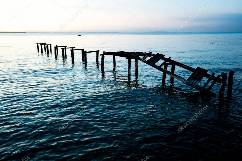 An old ramshackle pier with broken boards, during a beautiful sunset on a quiet lake.