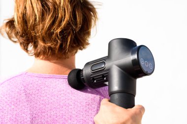 Kadın omuzlarında perküsyon tabancasıyla masaj uyguluyor, beyaz arka planda izole edilmiş..