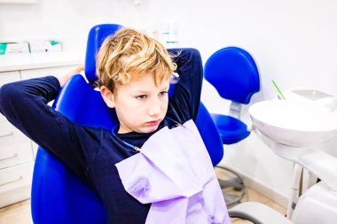 Bir çocuk diş muayenesi için dişçi koltuğunda endişeli bir suratla bekliyor..