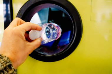 Adam ödül karşılığında geri dönüşüm makinesine plastik şişe koyuyor..