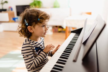 Sevimli küçük kız piyanonun başında oturmuş gülümserken notalarla deney yapıyor..