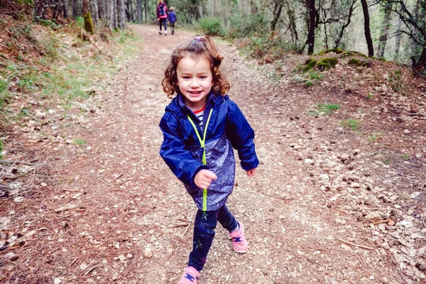 Komik küçük kız sonbaharda bir aile yürüyüşü yaparak ormanda yürüyor..