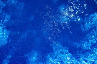 Şeffaf suları ve mavimsi arka planı olan bir yüzme havuzunun dalgalı yüzeyi..