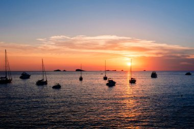 Güneşli sıcak bir gün batımı denizin yüzeyine yansıyor, körfezin yanında teknelerle..