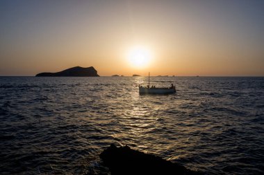 Kıyıya yakın birkaç tekne ve yat Akdeniz adalarının ufuklarında gün batımını seyrediyor..