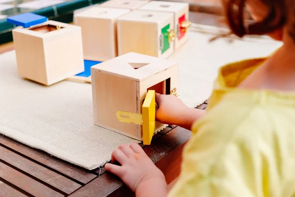 Little girl plays with a montessori educational material to open and close wooden boxes.