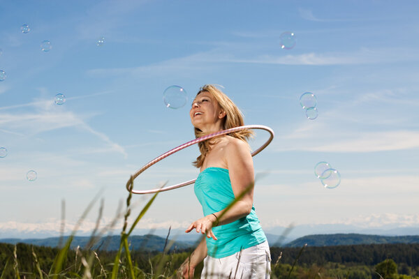 Blonde woman with soap bubbles and hula hoop in front of meadow