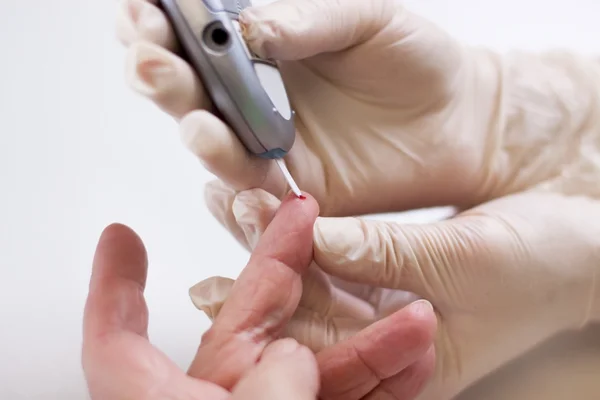 Geriatric nurse measures the blood sugar level — Stok fotoğraf