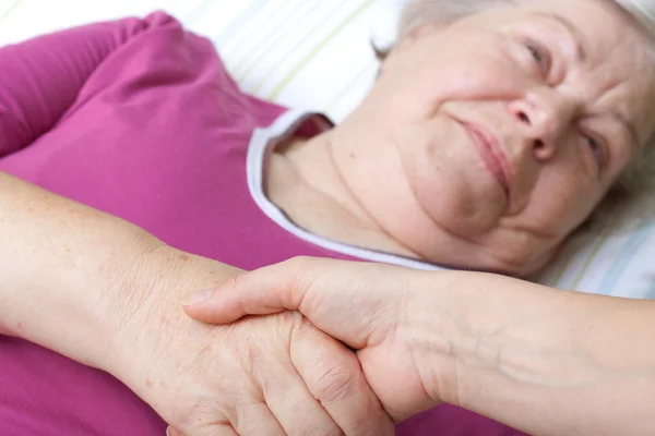 Senior lying in bed and welcomes nurse — стоковое фото