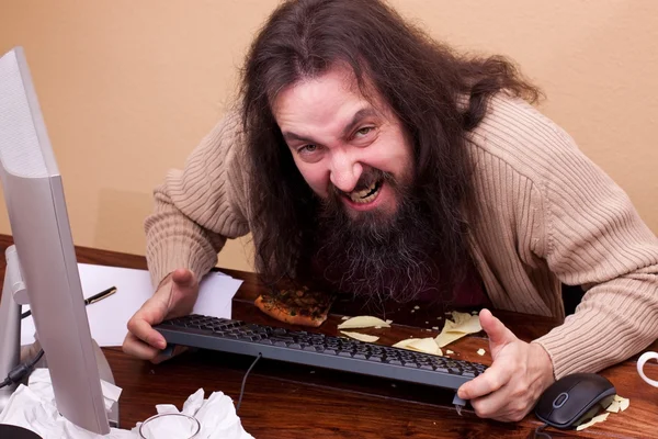 Angry nerd at a desk looking at viewer — Stock Photo, Image