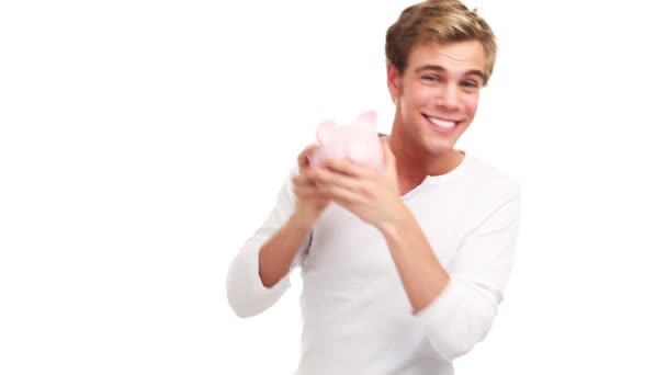 Радостный молодой человек держит копилку и трясет деньгами, смеется и улыбается. — стоковое видео