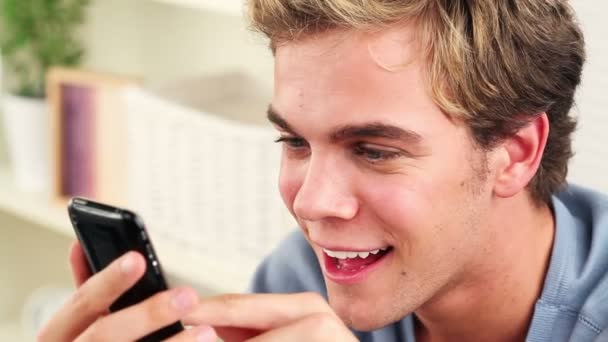 Радостный молодой человек, использующий мобильный телефон для отправки текстовых сообщений — стоковое видео