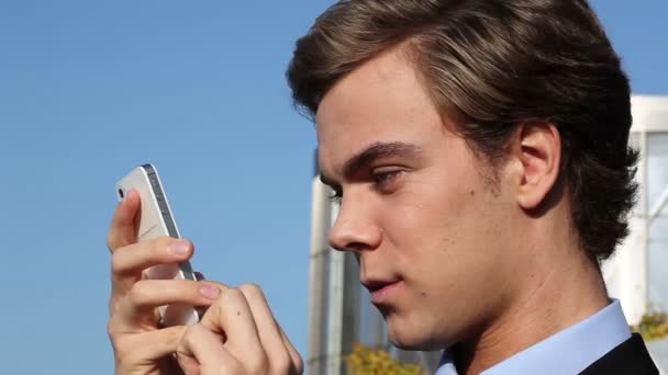 Attractive young businessman sending text message on mobile phone outdoors — Stock Video