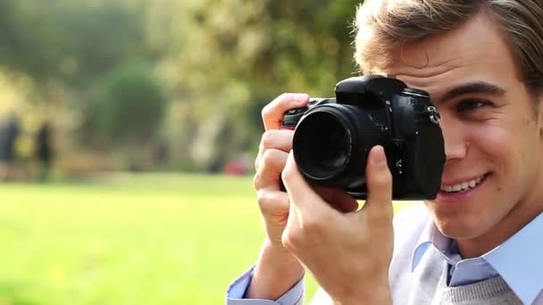 Привлекательный молодой фотограф-мужчина с помощью цифровой камеры dslr фотографирует на открытом воздухе в парке под солнцем — стоковое видео