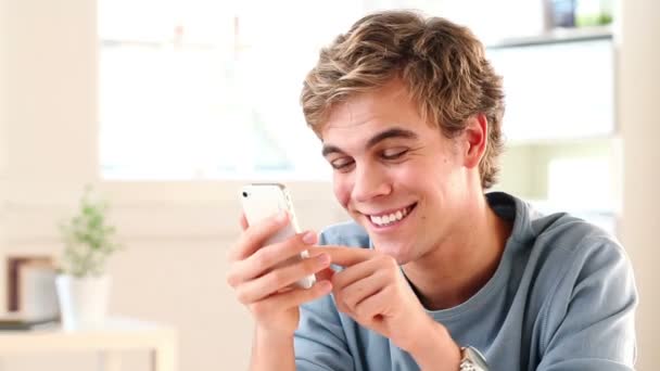 Радостный молодой человек отправляет смс с помощью смартфона - в помещении — стоковое видео