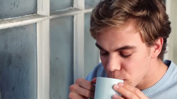 Attractive young man drinking coffee at window — Stock Video