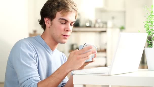 Привлекательный молодой студент, использующий мобильный телефон и ноутбук в помещении — стоковое видео