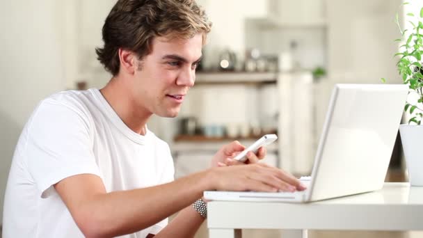 Giovane studente gioioso che parla sul telefono cellulare utilizzando il computer portatile a casa — Video Stock