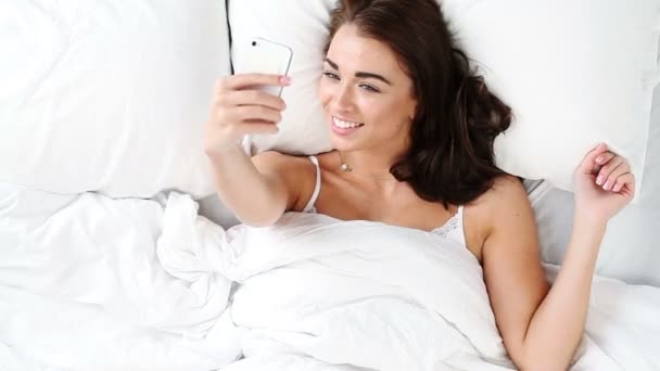 Cute young teenager girl in bed taking photos with mobile phone — Stock Video