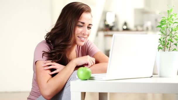 Joyeux jeune femme bavarder avec son petit ami sur Internet à la maison en utilisant un ordinateur portable et manger de la pomme verte — Video