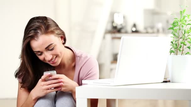 Красива молода жінка надсилає текстове повідомлення за допомогою мобільного телефону в приміщенні вдома, посміхаючись дивитися на камеру — стокове відео