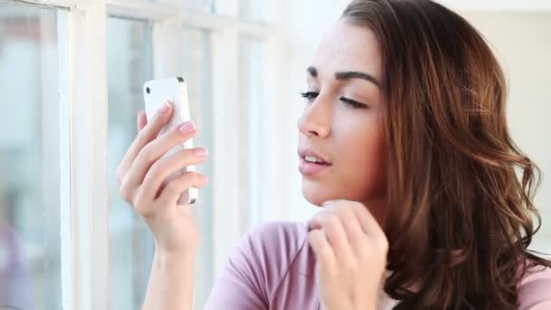 Young woman grooming herself using mobile phone as a mirror — Wideo stockowe