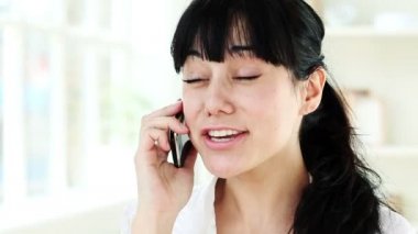 Evde cep telefonuyla konuşan mutlu genç bir kadın.