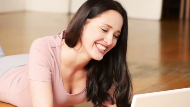 Attractive woman chatting on her laptop lying on the floor at home — Stock Video